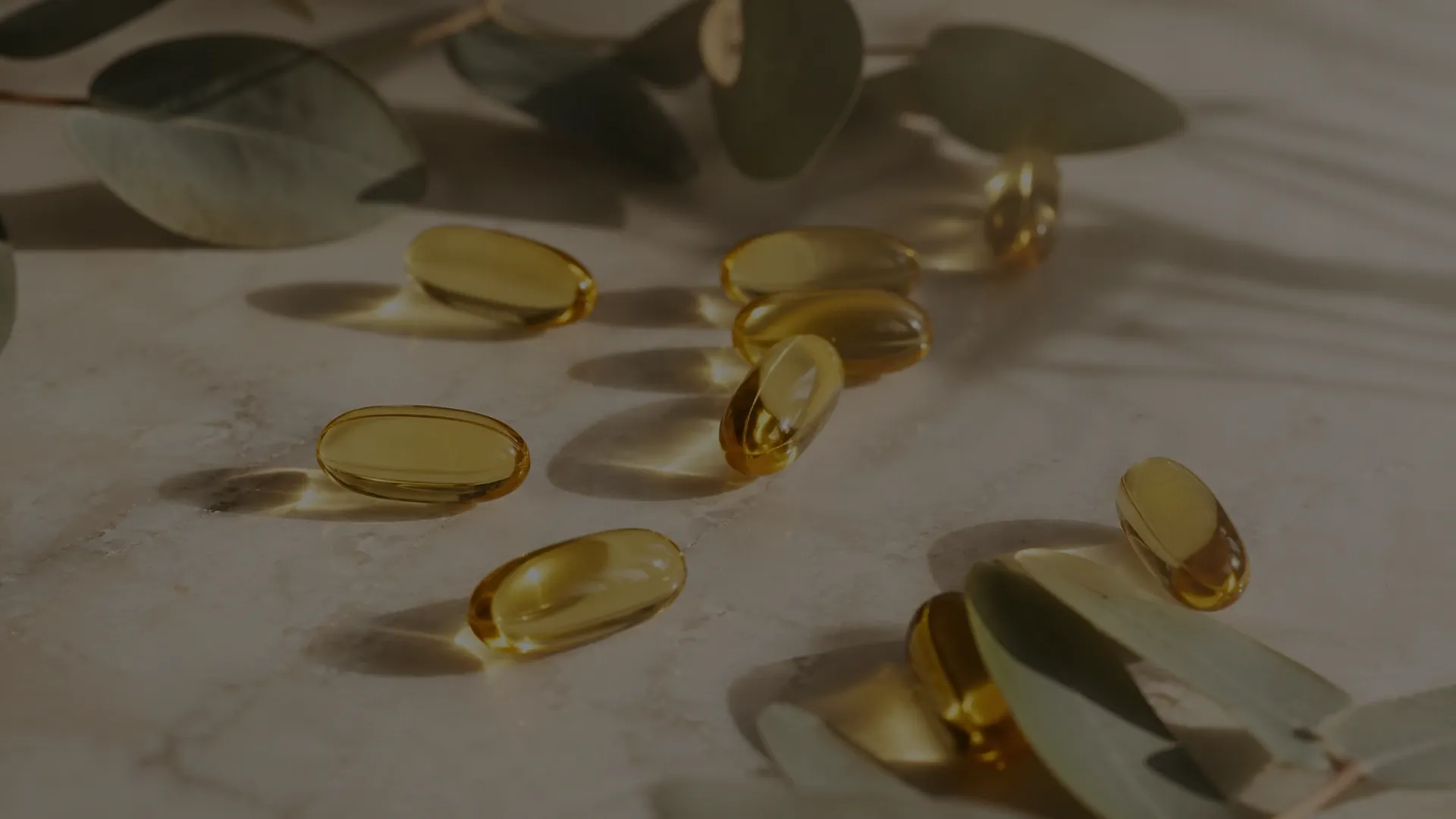 Goldene Omega-3-Kapseln auf hellem Marmor zwischen Eukalyptuszweigen