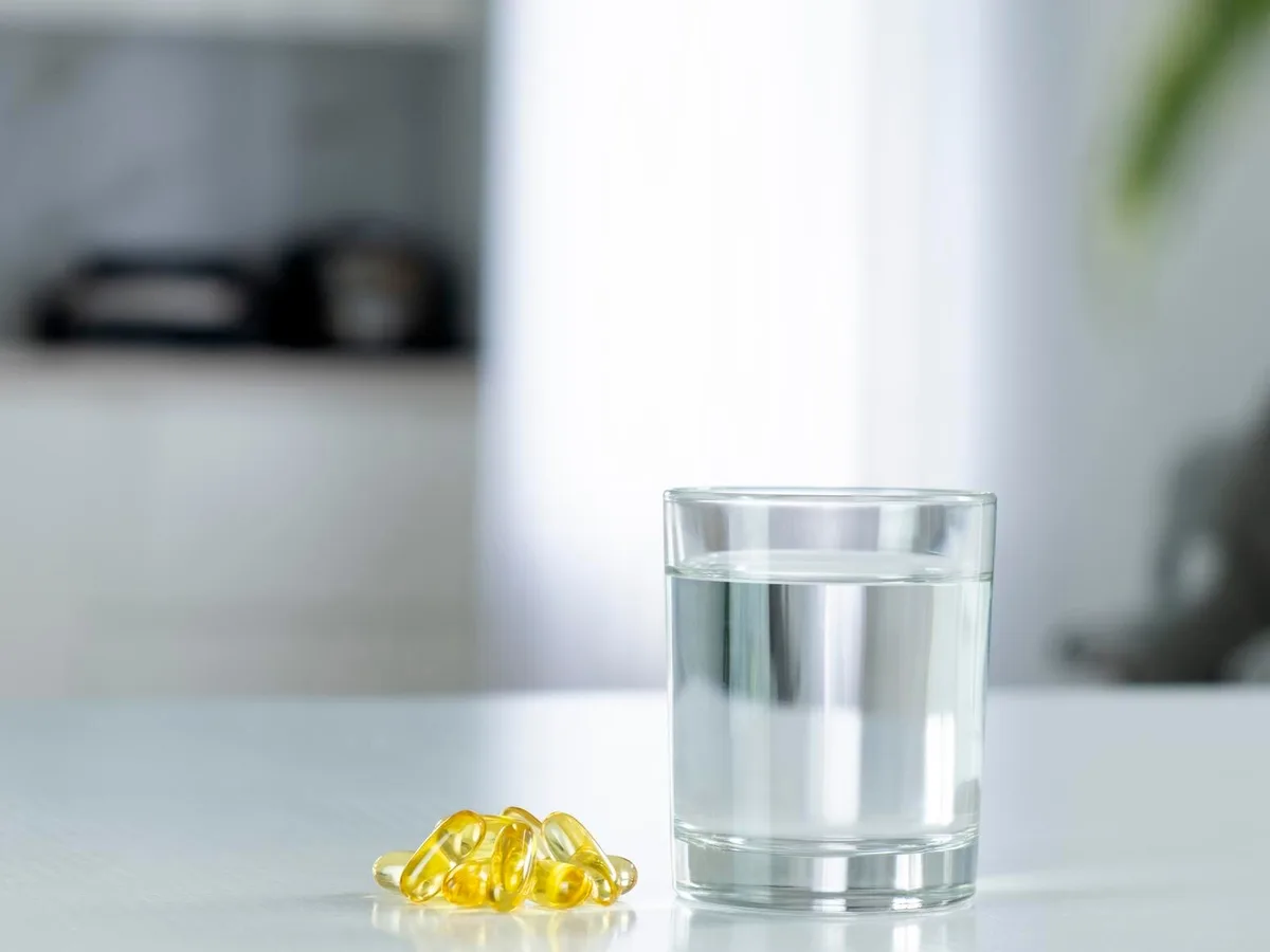 Omega-3-Kapseln und Wasserglas im Wohnzimmer