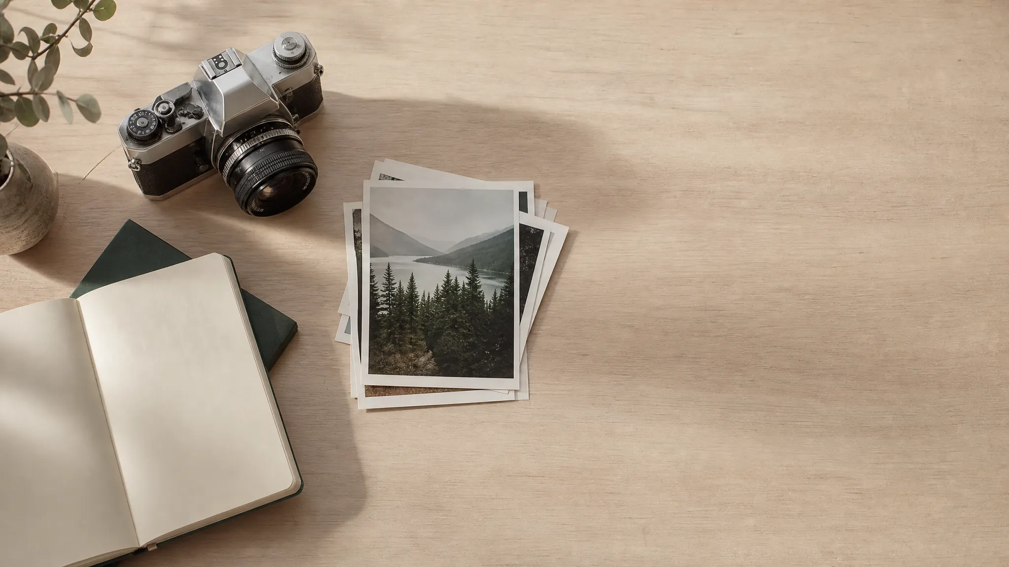 Analoge Kamera, gedruckte Fotoabzüge und ein Notizheft auf einem hellen Holztisch