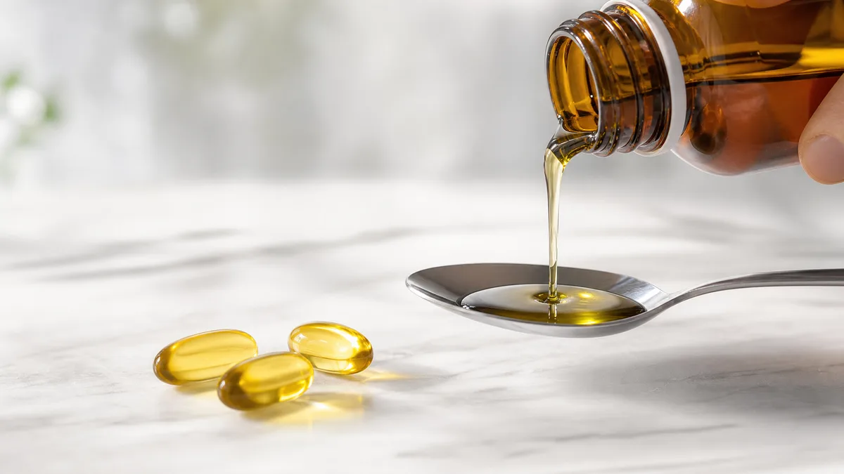 Fl&uuml;ssiges Omega-3-&Ouml;l wird in einen L&ouml;ffel dosiert, daneben Kapseln