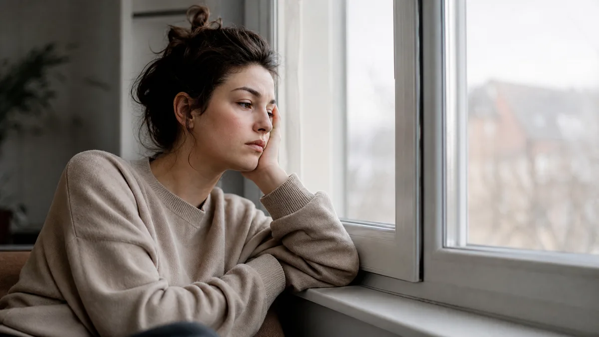 M&uuml;de Frau am Fenster im gedämpften Tageslicht