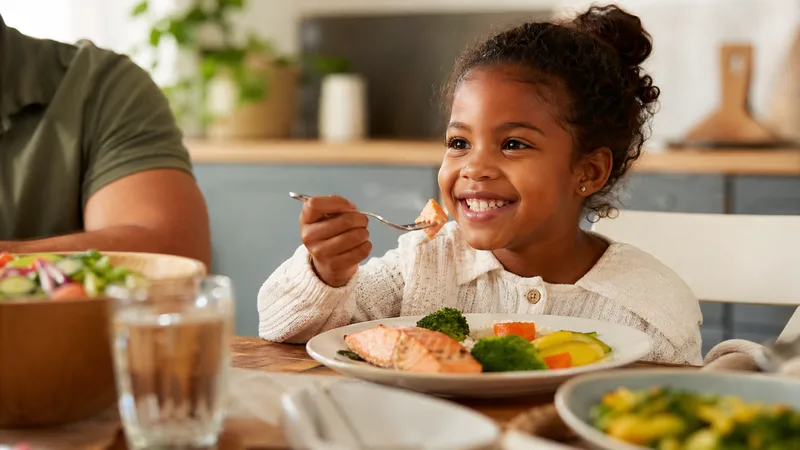 Kind isst gesunden Lachs am Familientisch